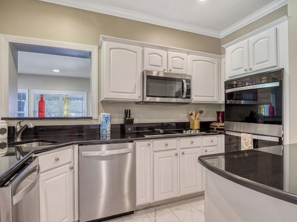 A modern kitchen with stainless steel appliances, white cabinetry, and a black countertop.