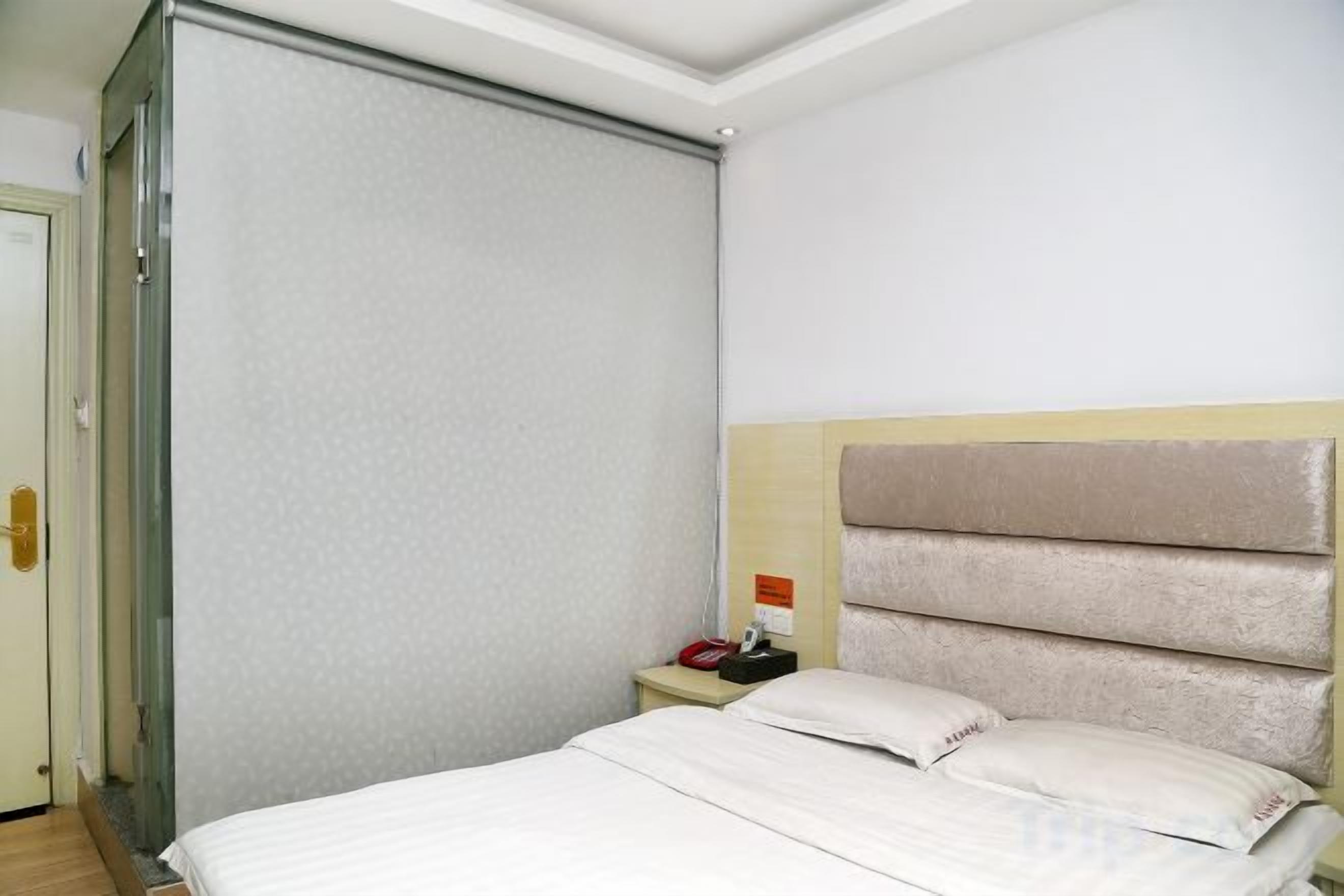 A hotel room with a bed, a nightstand, and a door.