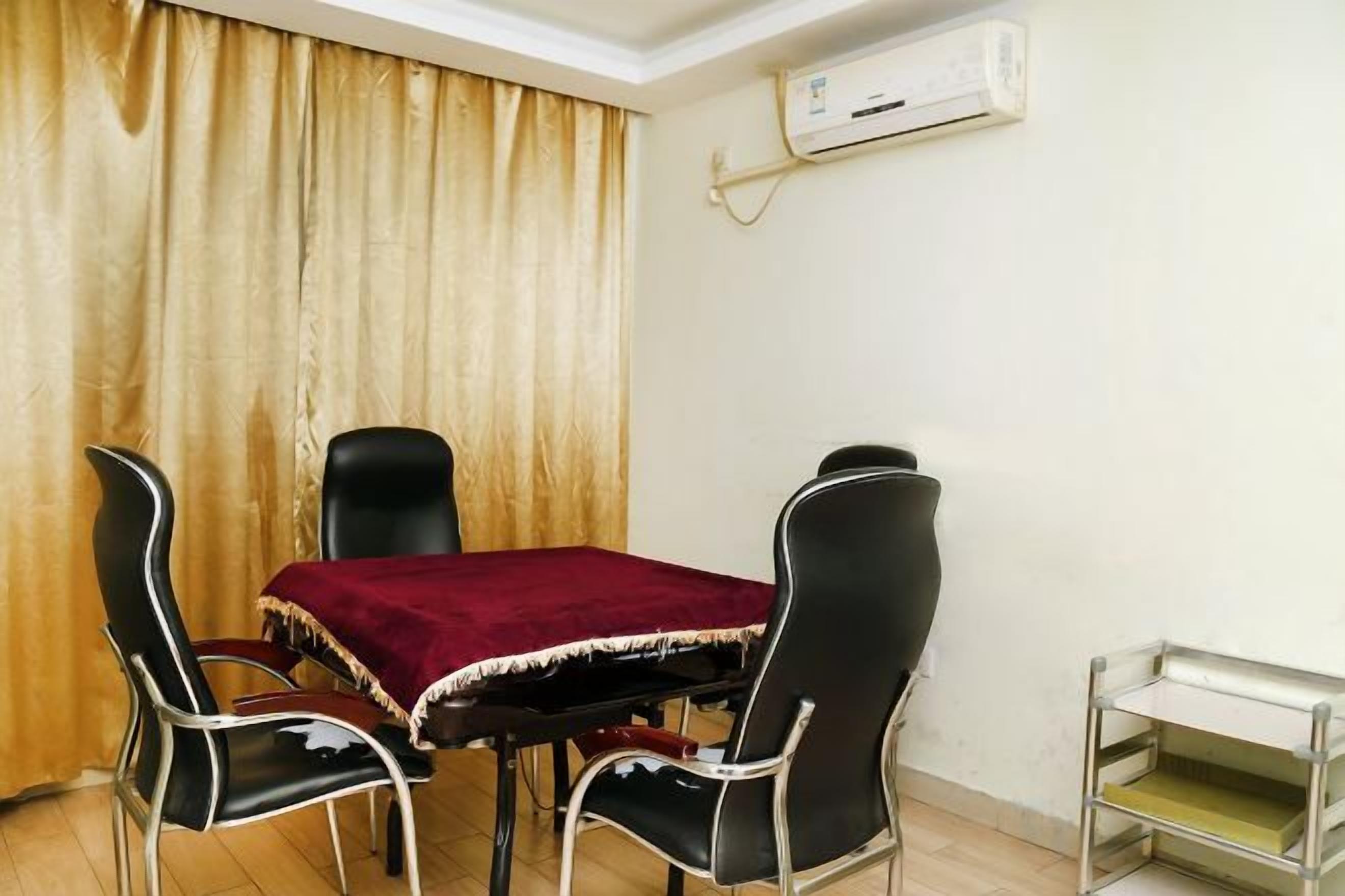 A dining area with a table and four chairs, an air conditioning unit on the wall, and a small metal shelf.
