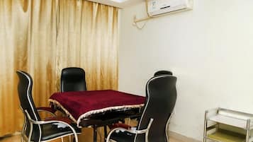 Un comedor con una mesa y cuatro sillas, un equipo de aire acondicionado en la pared y un estante metálico pequeño.