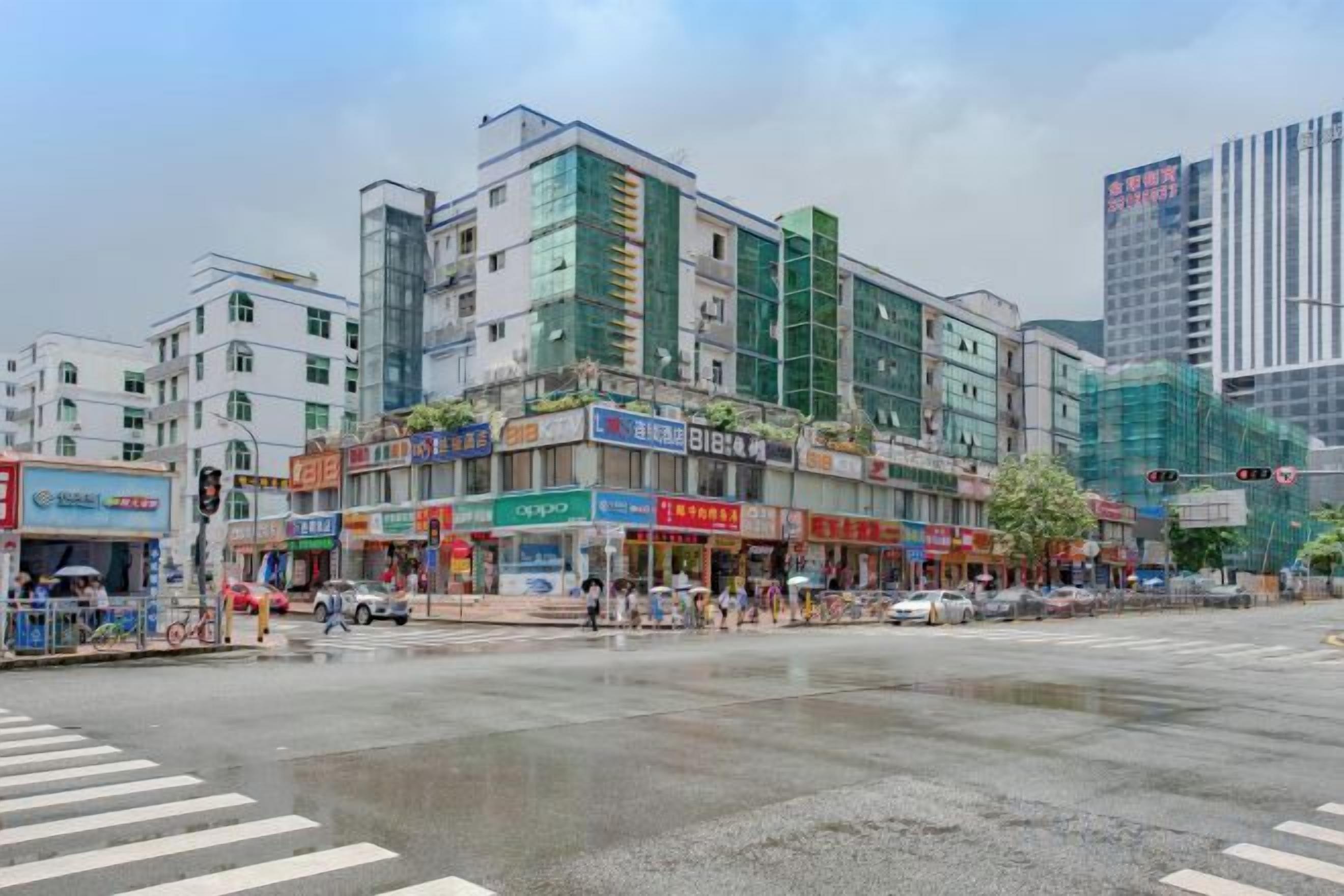 A multi-story building with commercial shops on the ground floor, a pedestrian crossing, and a wet street.