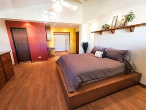 A bedroom with a bed, wooden floor, a ceiling fan, and a shelf with decorative items. - Playa Plateada Beach House (Ensenada)