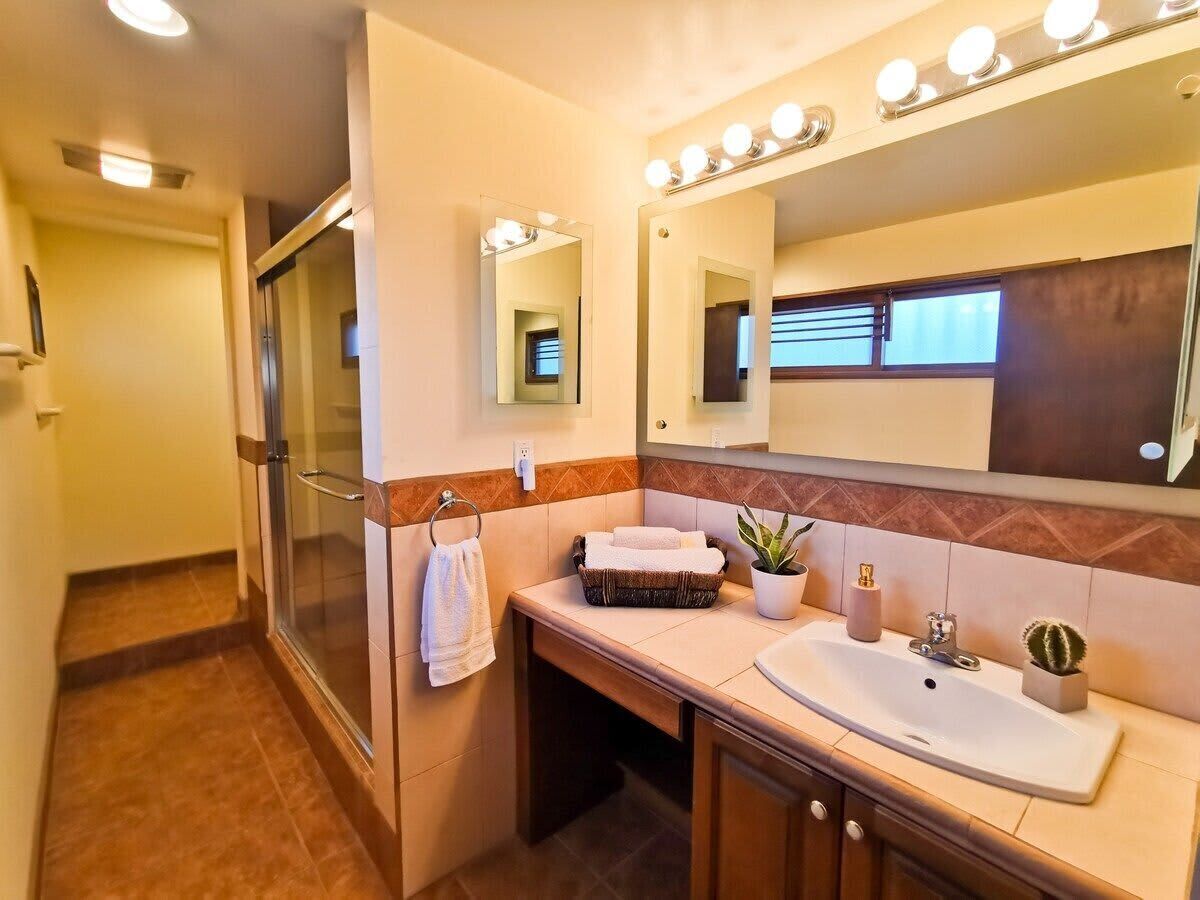 A bathroom with a glass shower, a vanity with a sink, a mirror with lights, and a towel rack.