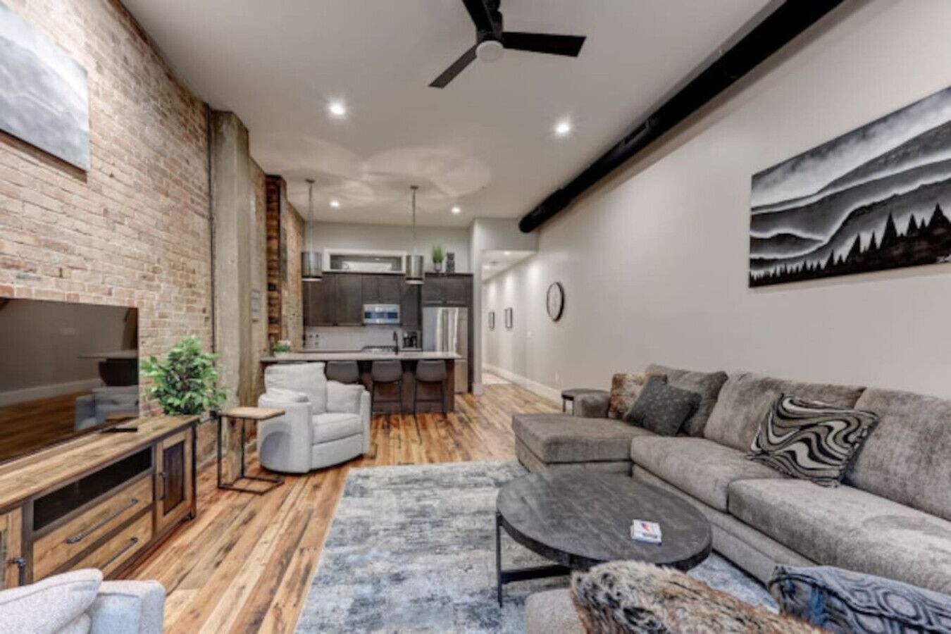 A modern living room with a sofa, coffee table, and TV. There is a kitchen in the background with a bar area.