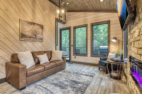 A cozy living room with a brown leather sofa, a large painting, and a stone fireplace. - Lullaby Falls- Hot Tub, Wifi, Near 75 ft Waterfall, Free Attraction Tickets!!! (Sevierville)