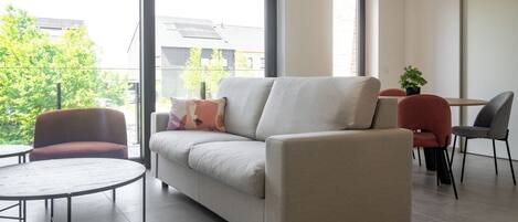 A modern living room with a sofa, two armchairs, a small table, and a potted plant.