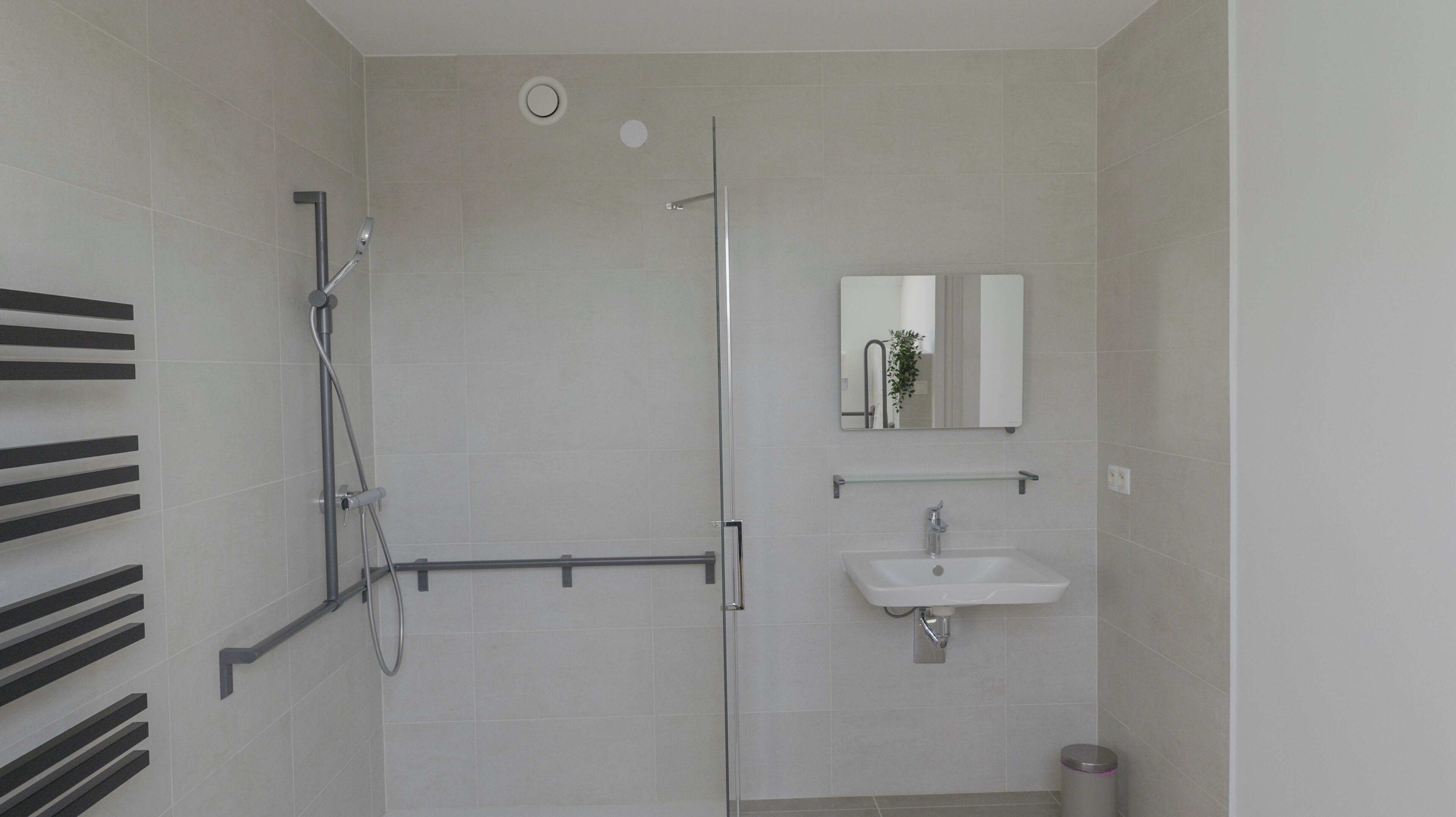Een moderne badkamer met een douchecabine van glas, een witte wastafel en een spiegel erboven.