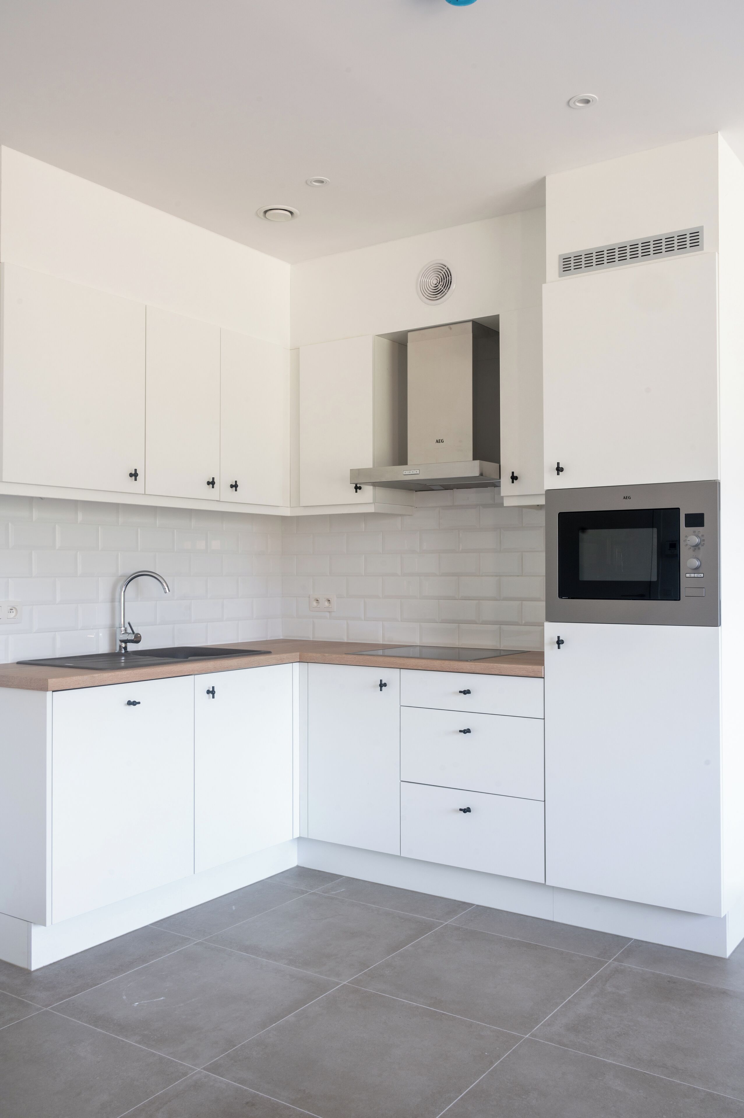 A modern kitchen with white cabinets, a built-in microwave, and a grey tiled backsplash.