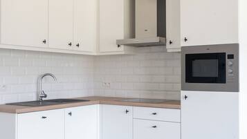 A modern kitchen with white cabinets, a built-in microwave, and a grey tiled backsplash.