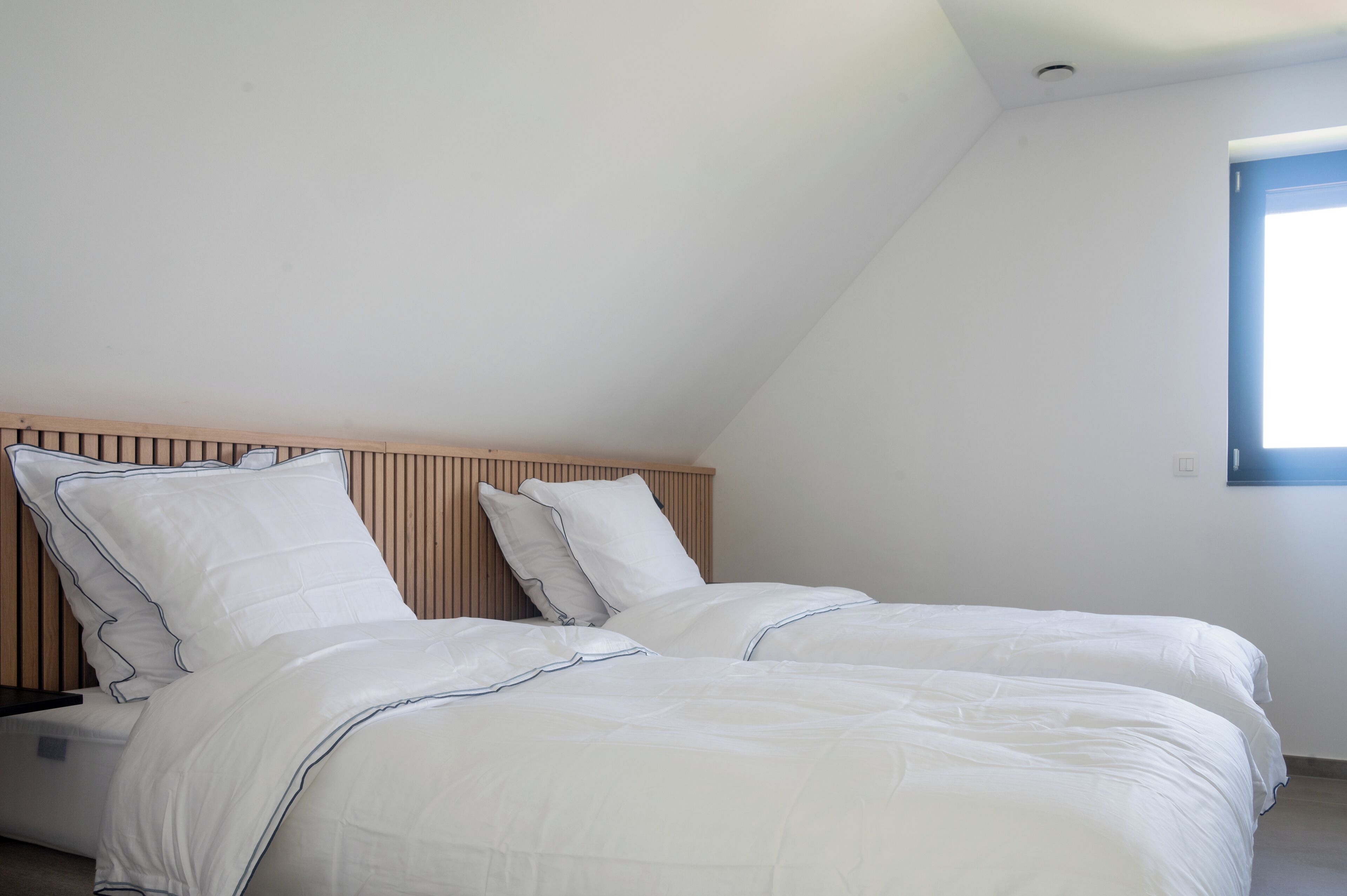 A bedroom with two beds, wooden headboard, white bedding, and a window with natural light.