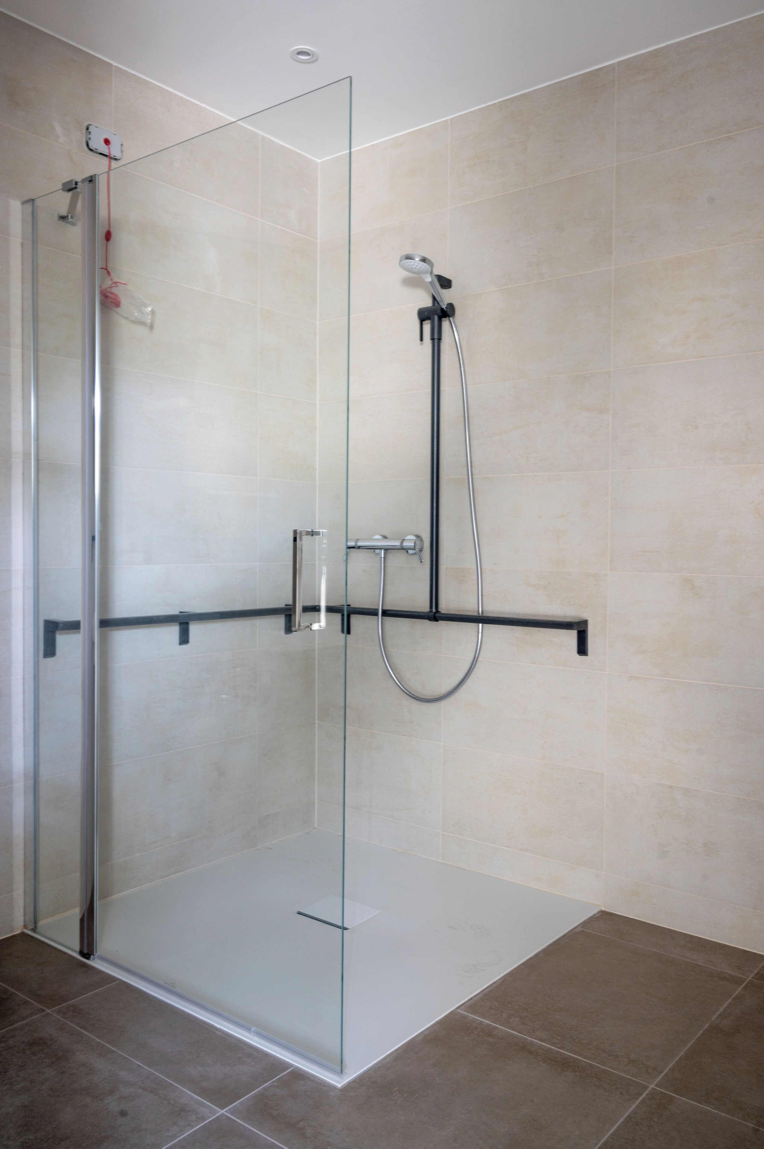 A modern shower enclosure with a glass door, a handheld showerhead, and a wall-mounted control panel.
