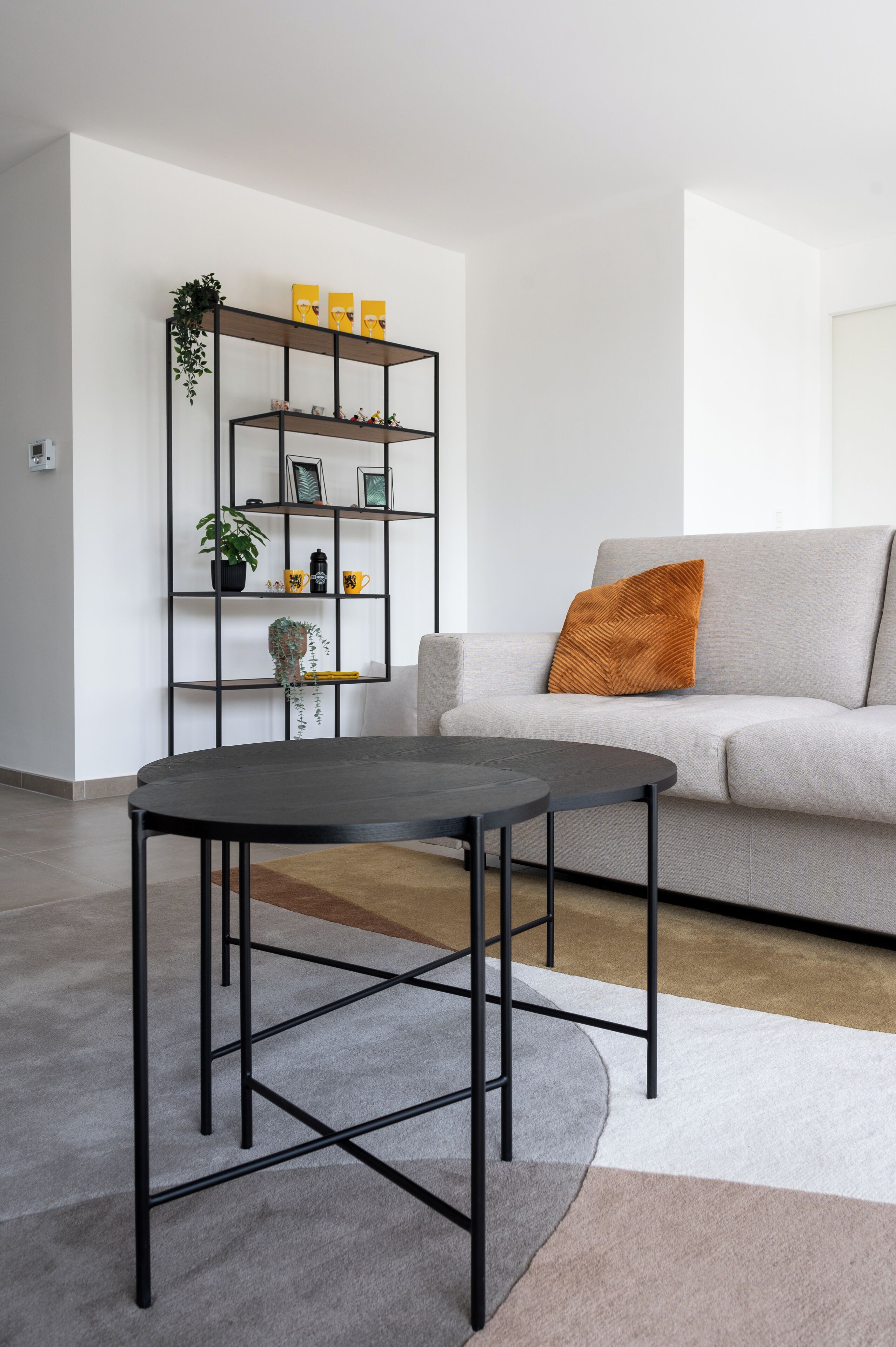 En moderne stue med en grå sofa, et sort sofabord og et sort metalreol med pynteting.