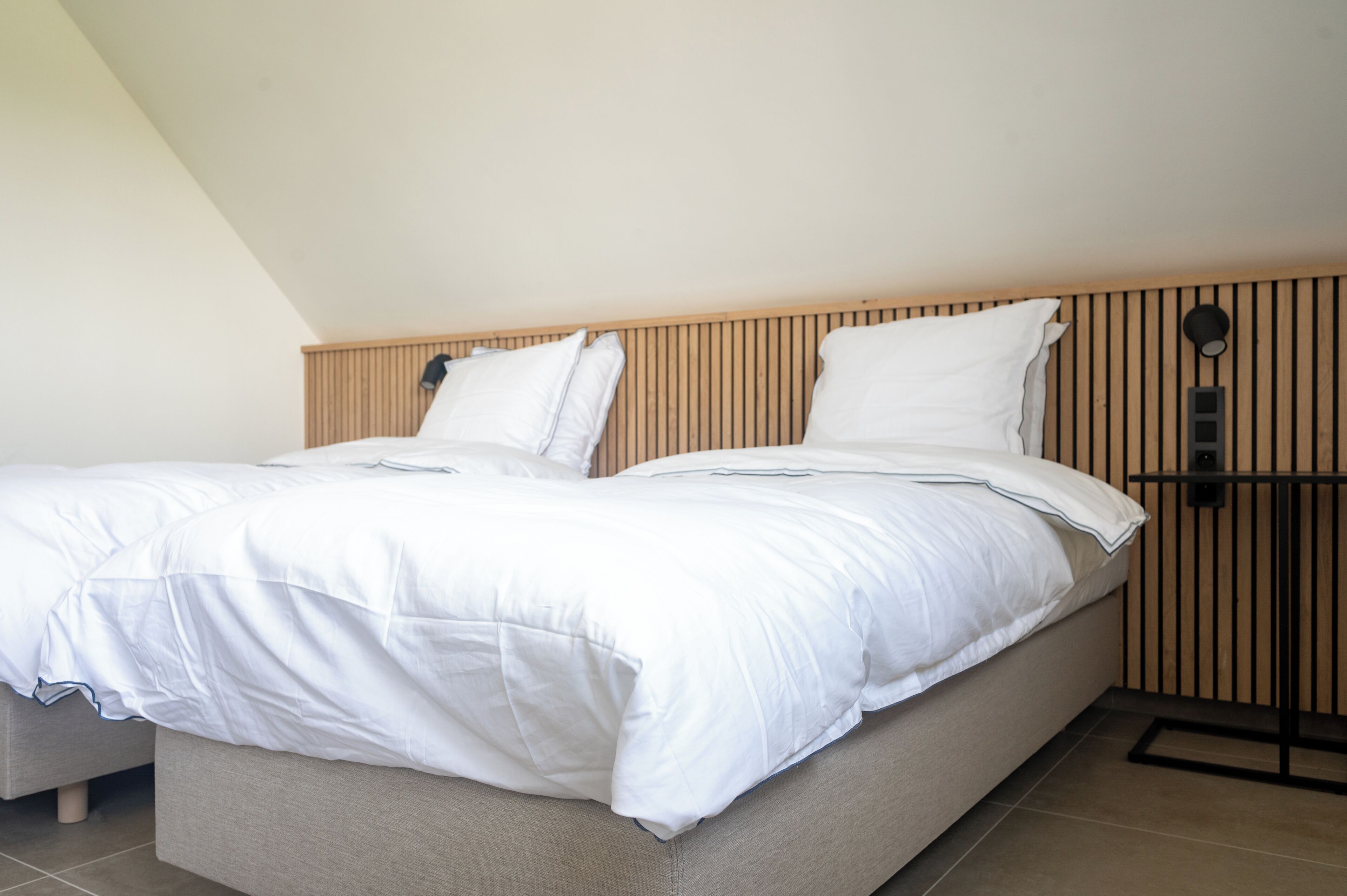 A double bed with white bedding in a room with wooden slatted headboard and a black nightstand.
