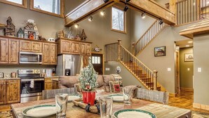 A spacious kitchen with wooden cabinets, a dining area with a table set for four, and a staircase leading to an upper level.