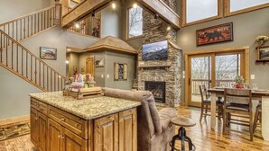 A spacious living area with a stone fireplace, wooden staircase, and a cozy seating area.