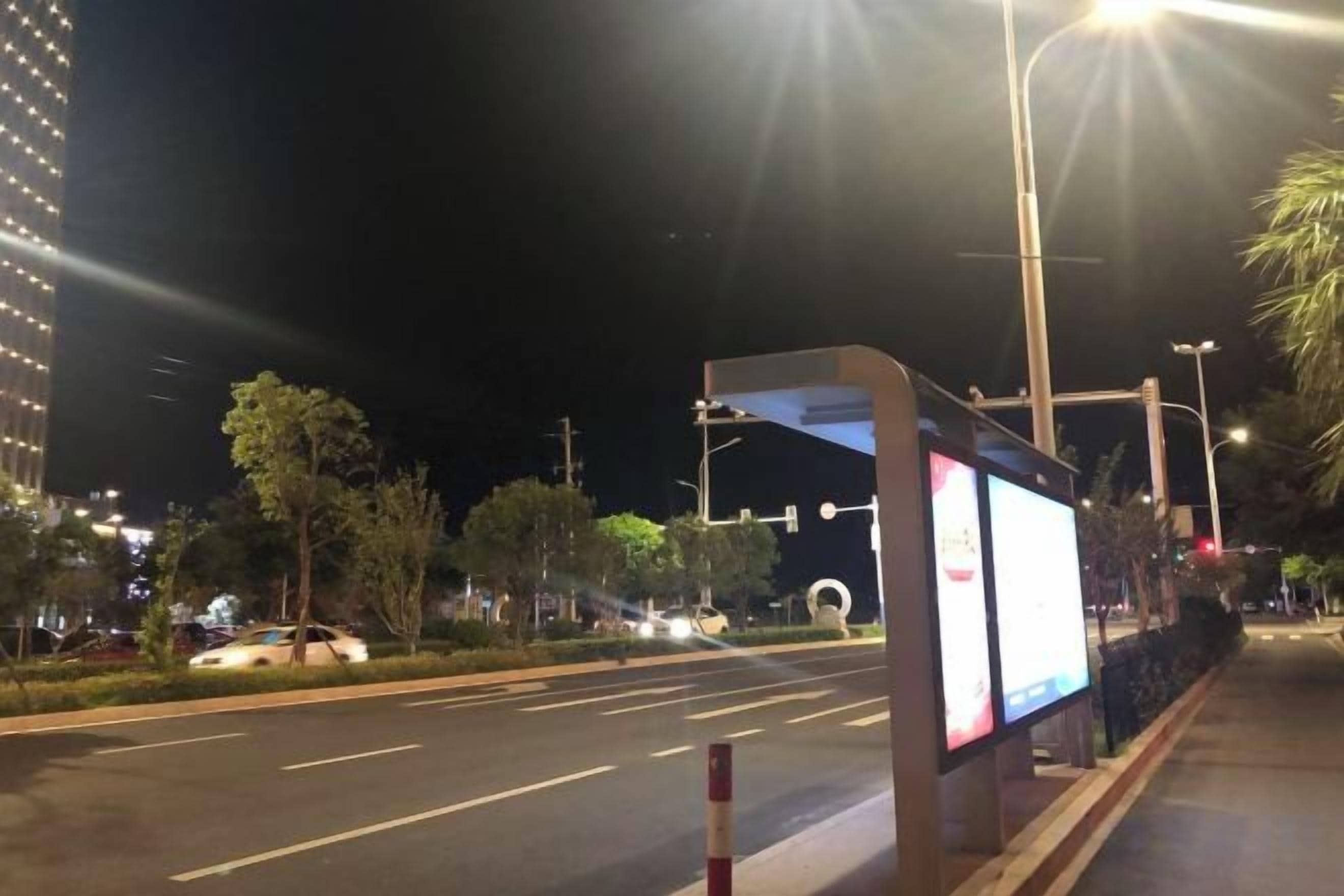 A nighttime street scene with a road, streetlights, and a digital billboard.