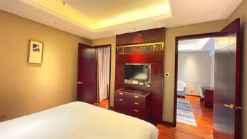 A hotel room with a bed, a dresser, a television, and a door leading to another room.