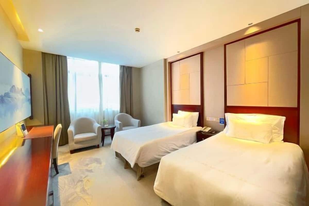 A hotel room with two beds, a desk, a chair, and a large window.