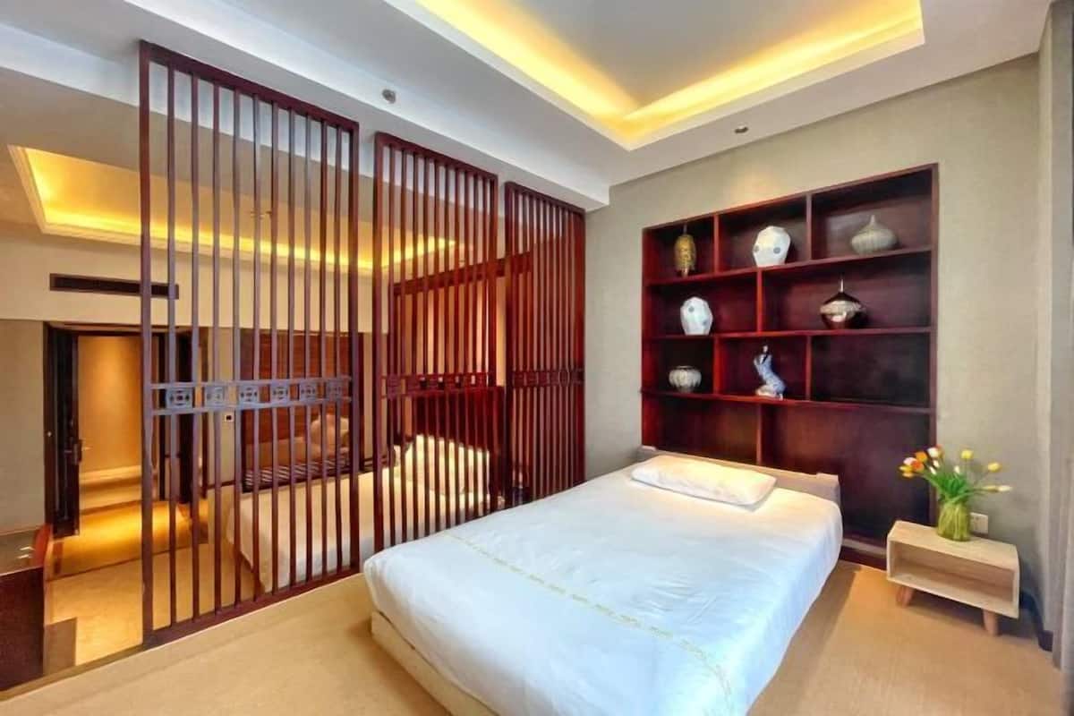 A bedroom with a bed, a wooden partition, a shelf with decorative items, and a nightstand with a vase.