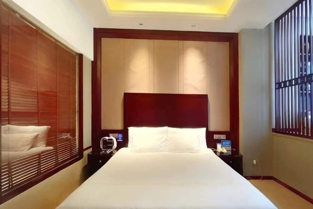 A hotel room with a large bed, wooden headboard, bedside tables, and a window with bars.