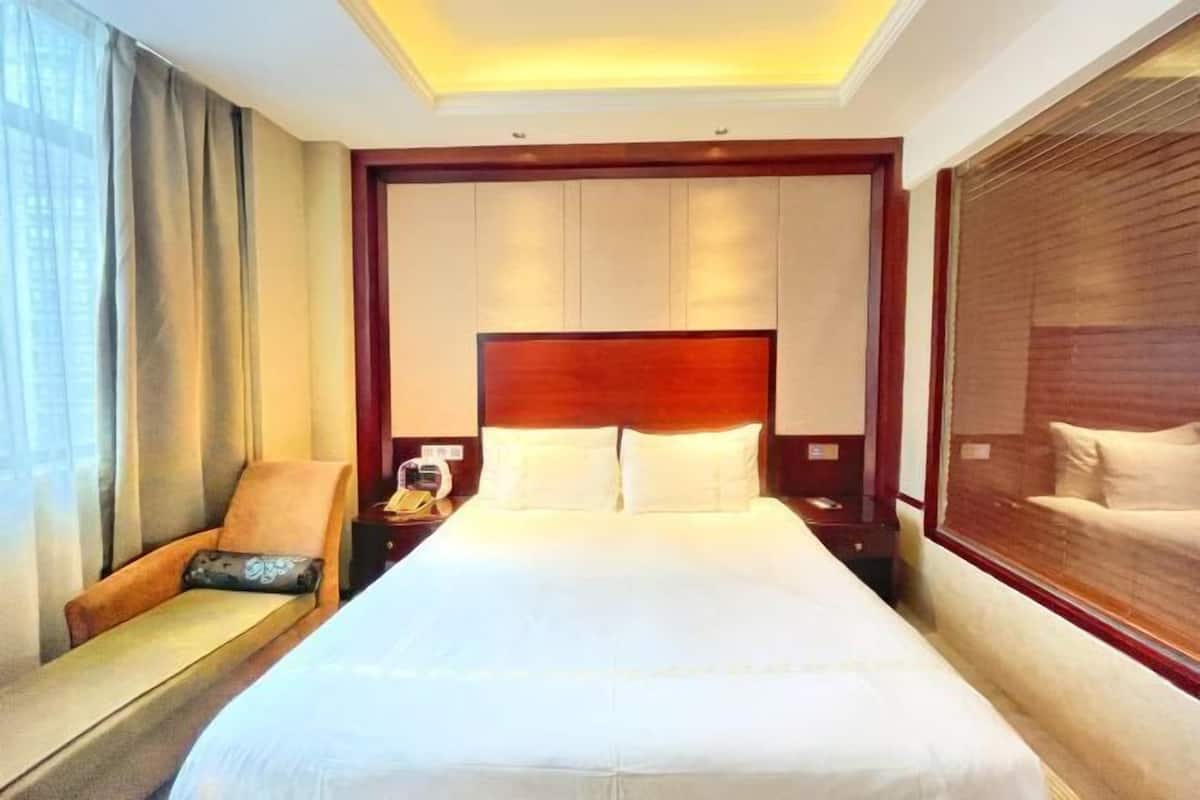 A hotel room with a large bed, a nightstand, a chair, and a window with blinds.