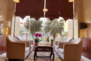A hotel lobby with leather armchairs, a wooden coffee table, and a view of palm trees and buildings.
