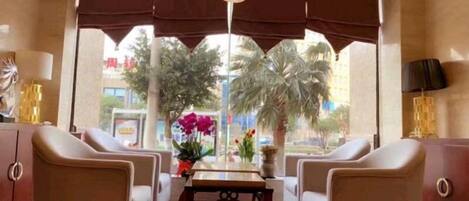 A hotel lobby with two sofas, a table, and a view of palm trees and buildings.