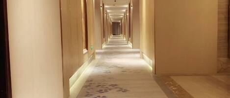 A long, narrow hotel corridor with a patterned carpet and doors on both sides.