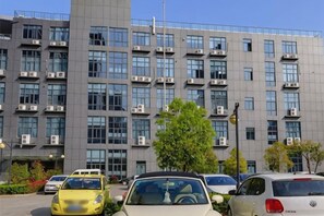 A multi-story building with air conditioning units, a parking lot with cars, and a tree in the foreground. - Royal Regent Hotel (Yuhuan)