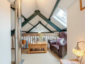 A cozy loft bedroom with a sloped ceiling, a wooden table, a leather armchair, and a decorative lamp. - Rhydyfran Coach House (Cribyn, near Lampeter)