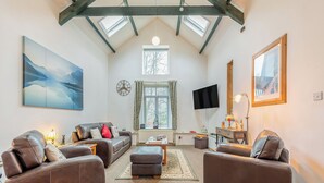A spacious living room with a high ceiling, a large window, and a flat-screen TV mounted on the wall.