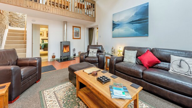 A spacious living area with a high ceiling, a wooden staircase, a fireplace, leather sofas, and a large painting.