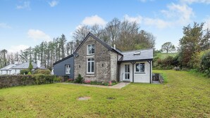 A stone house with a sloped roof, a small porch, and a grassy yard.
