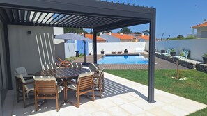 Une terrasse couverte avec une piscine, du mobilier d’extérieur et une vue sur les maisons voisines.