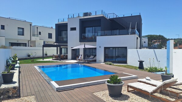 A modern two-story house with a swimming pool, outdoor seating, and a garden.