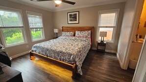 Quarto com cama, ventilador de teto, duas luminárias de cabeceira e janelas com persianas.