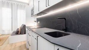 Een moderne keuken met een zwart marmeren aanrecht, een zwarte gootsteen en witte kastjes.