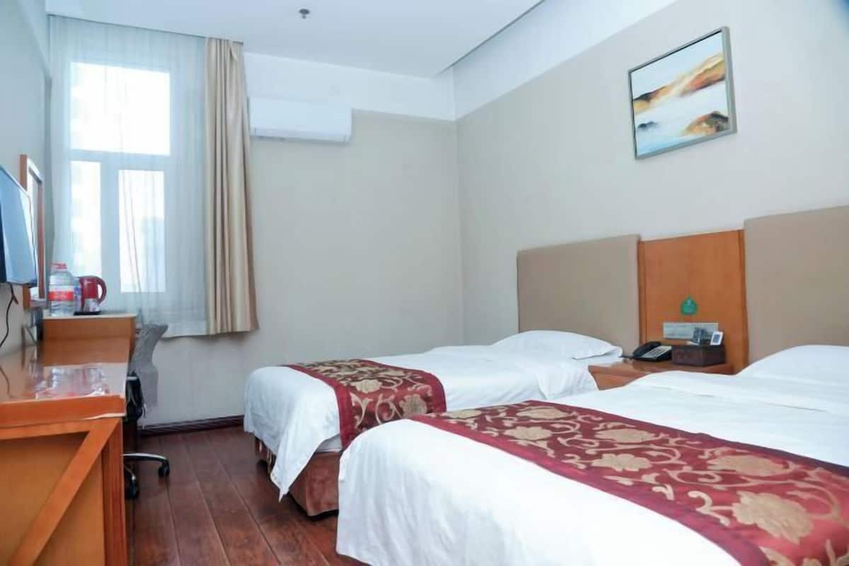 A hotel room with two beds, a desk, a chair, a TV, and a window with curtains.