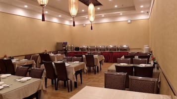 A conference room with tables and chairs, a stage with a red backdrop, and hanging lamps.