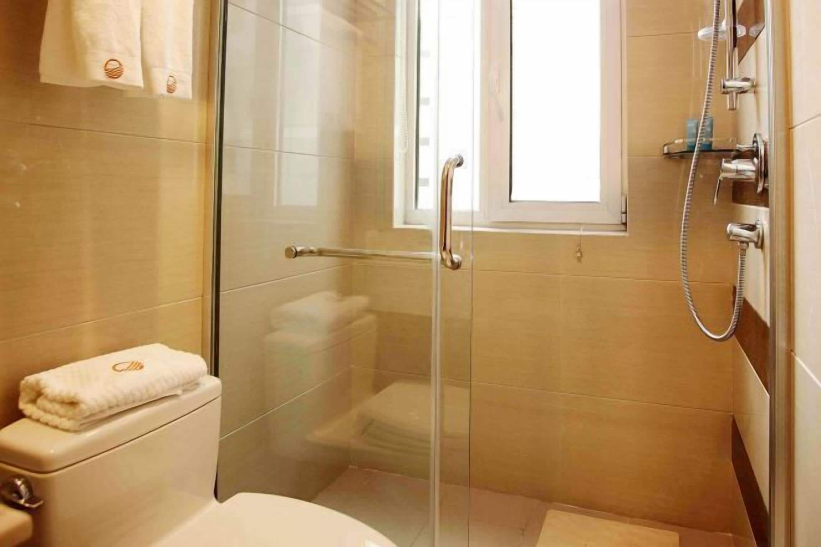 A glass-enclosed shower with a handheld showerhead, a toilet, and a window.