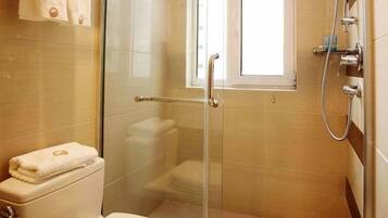 A glass-enclosed shower with a handheld showerhead, a toilet, and a window.