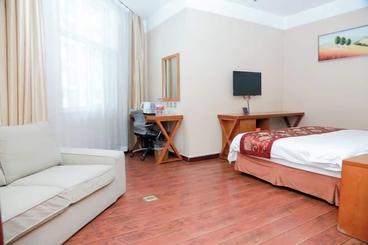 A hotel room with a sofa, a desk with a chair, a bed, a TV, and a painting on the wall.