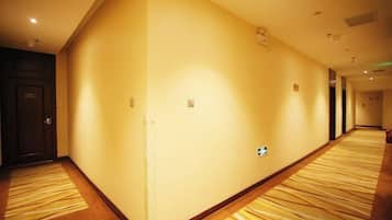 Un pasillo de hotel con pisos alfombrados, una puerta a la izquierda y un interruptor de luz en la pared.