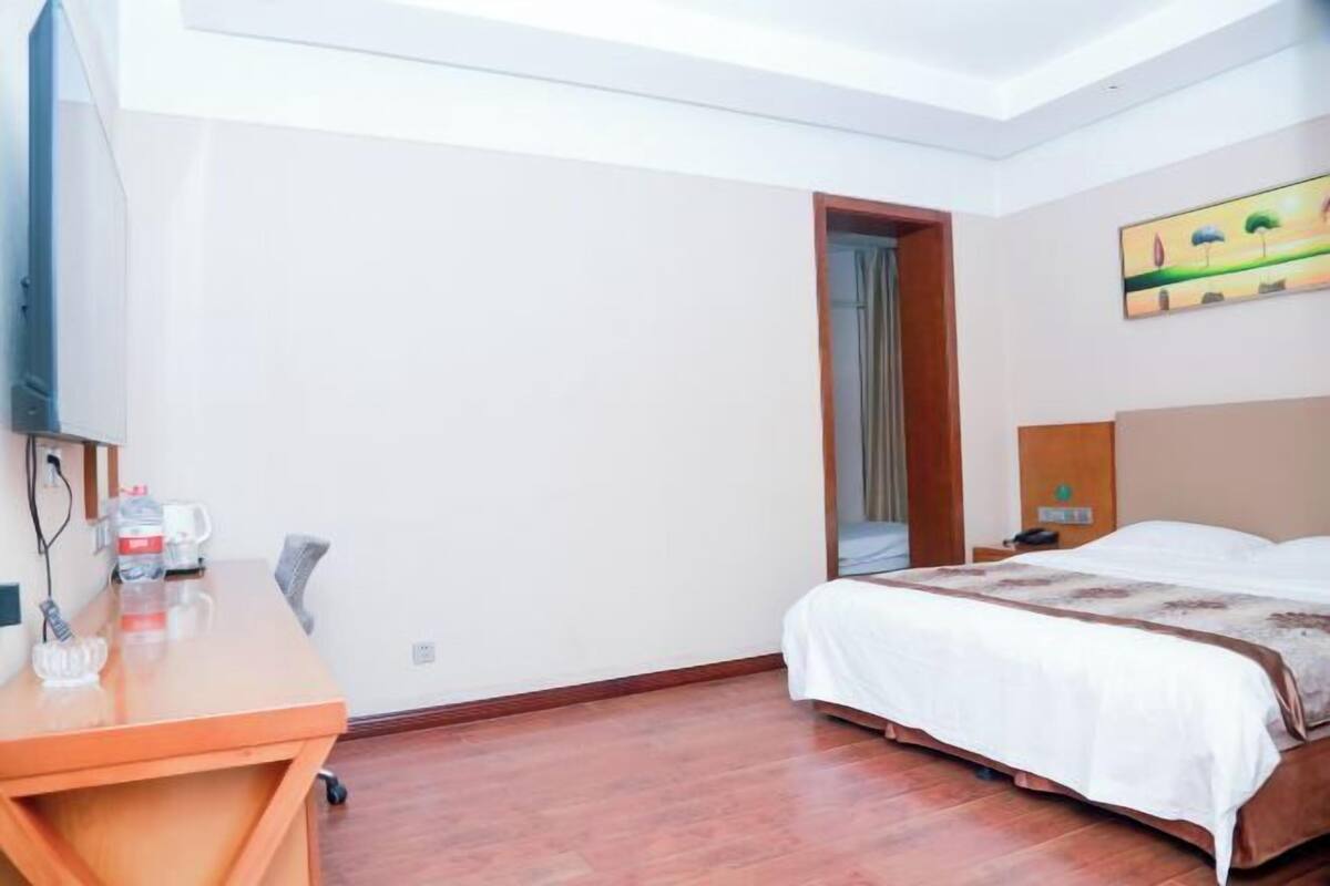 A hotel room with a bed, a desk, a chair, a TV, and a painting on the wall.