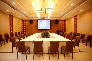 Un salón de conferencias con una larga mesa, sillas, una pantalla de proyector y una planta.