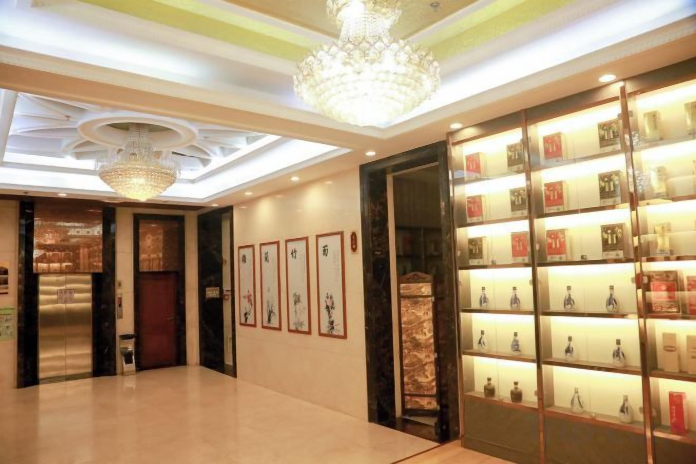 Um hall de hotel com um lustre, obras de arte emolduradas e uma exposição de garrafas.