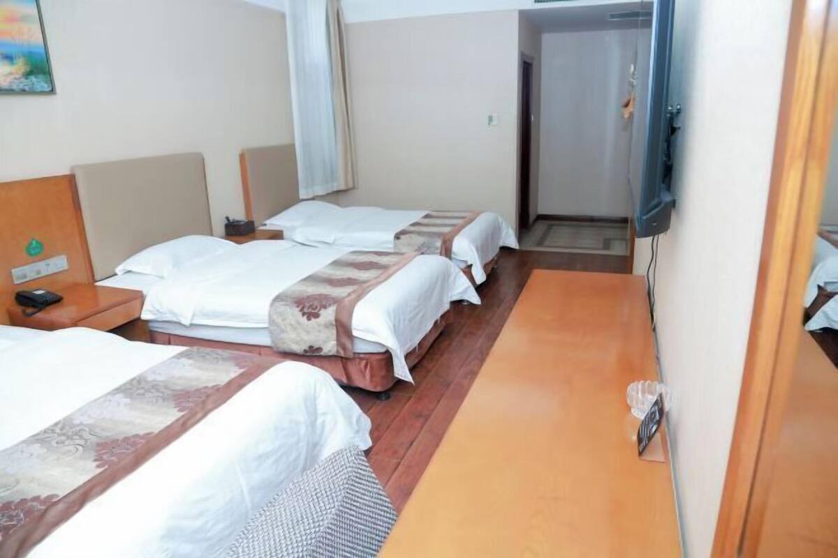 A hotel room with three beds, a wooden floor, a television, and a door leading to another room.