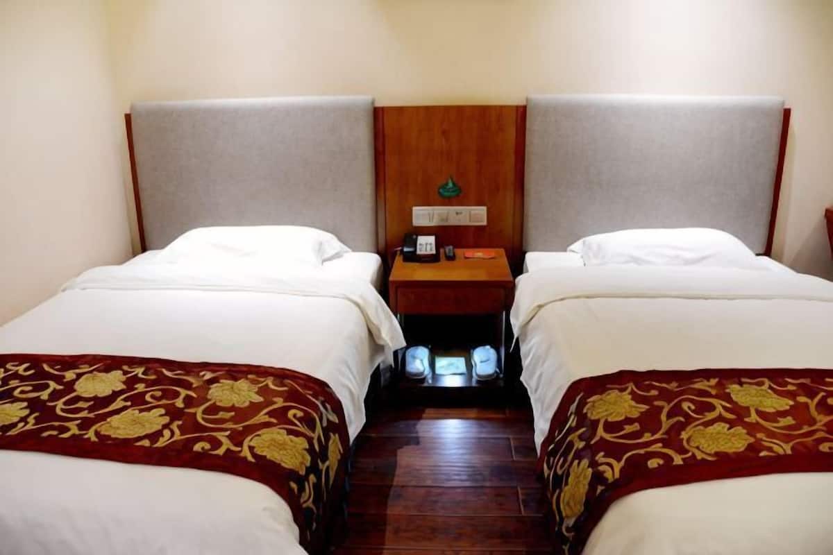 A hotel room with two single beds, a wooden headboard, a nightstand with a phone and lamp, and a small window.