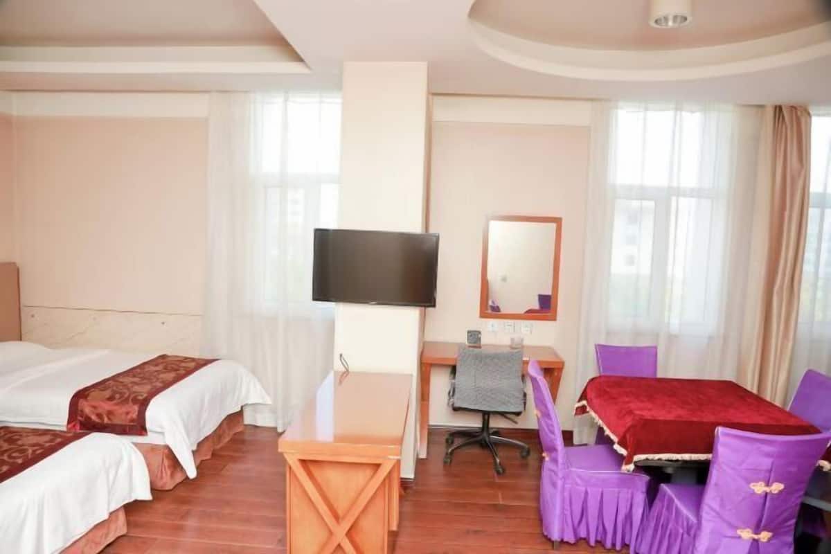 A hotel room with two beds, a desk with a chair, a TV, and a dining table with purple chairs.