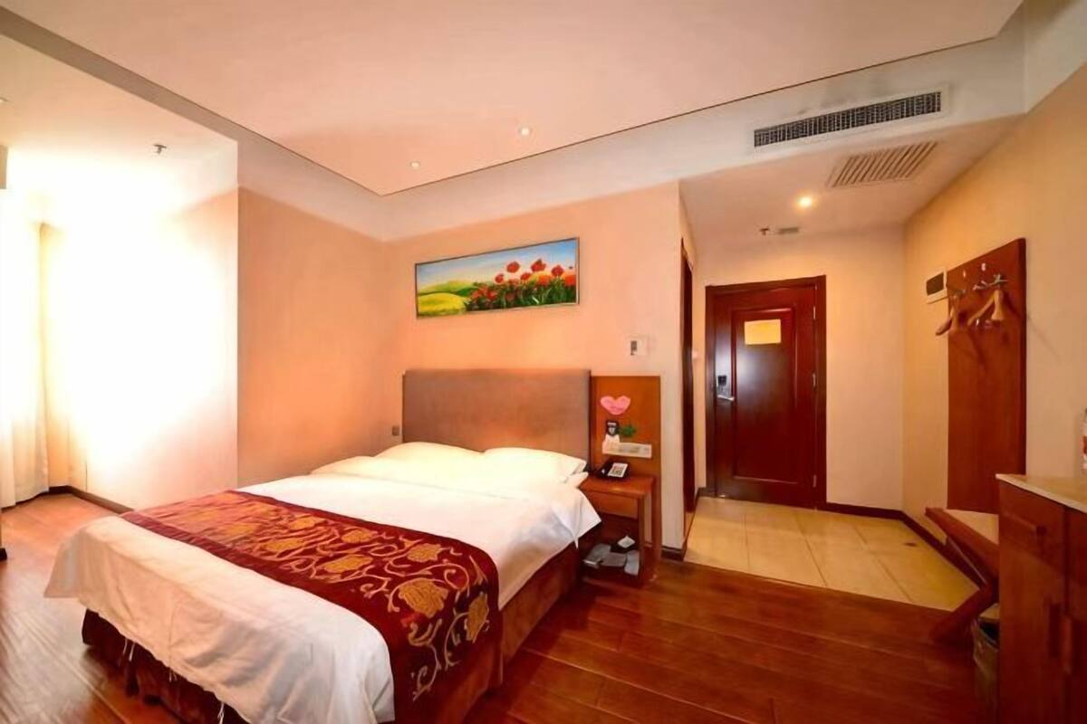 A hotel room with a bed, bedside table, lamp, painting, and a wooden wardrobe.